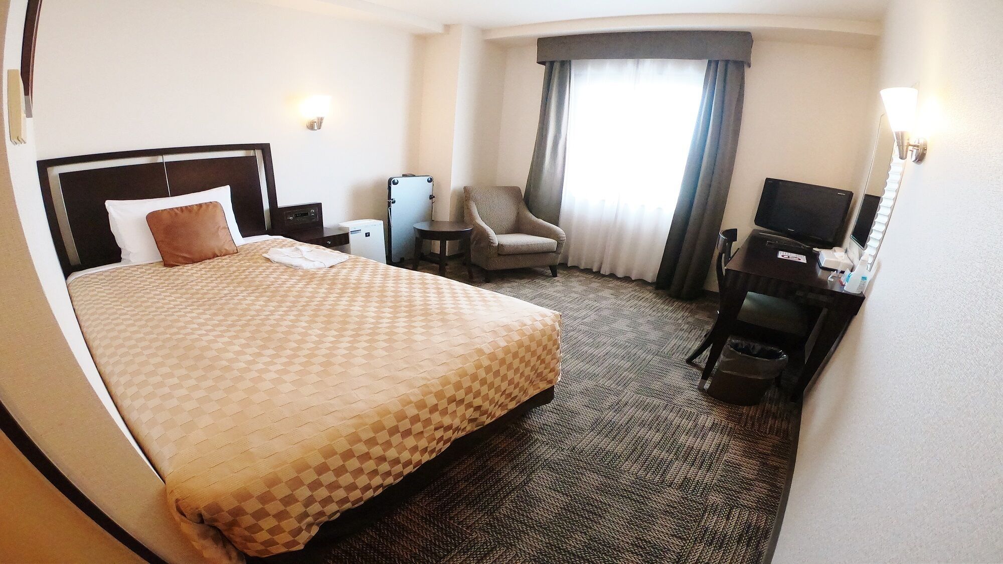 Une chambre d’hôtel avec un grand lit, une chaise, un bureau avec une télévision et une petite table avec une lampe.