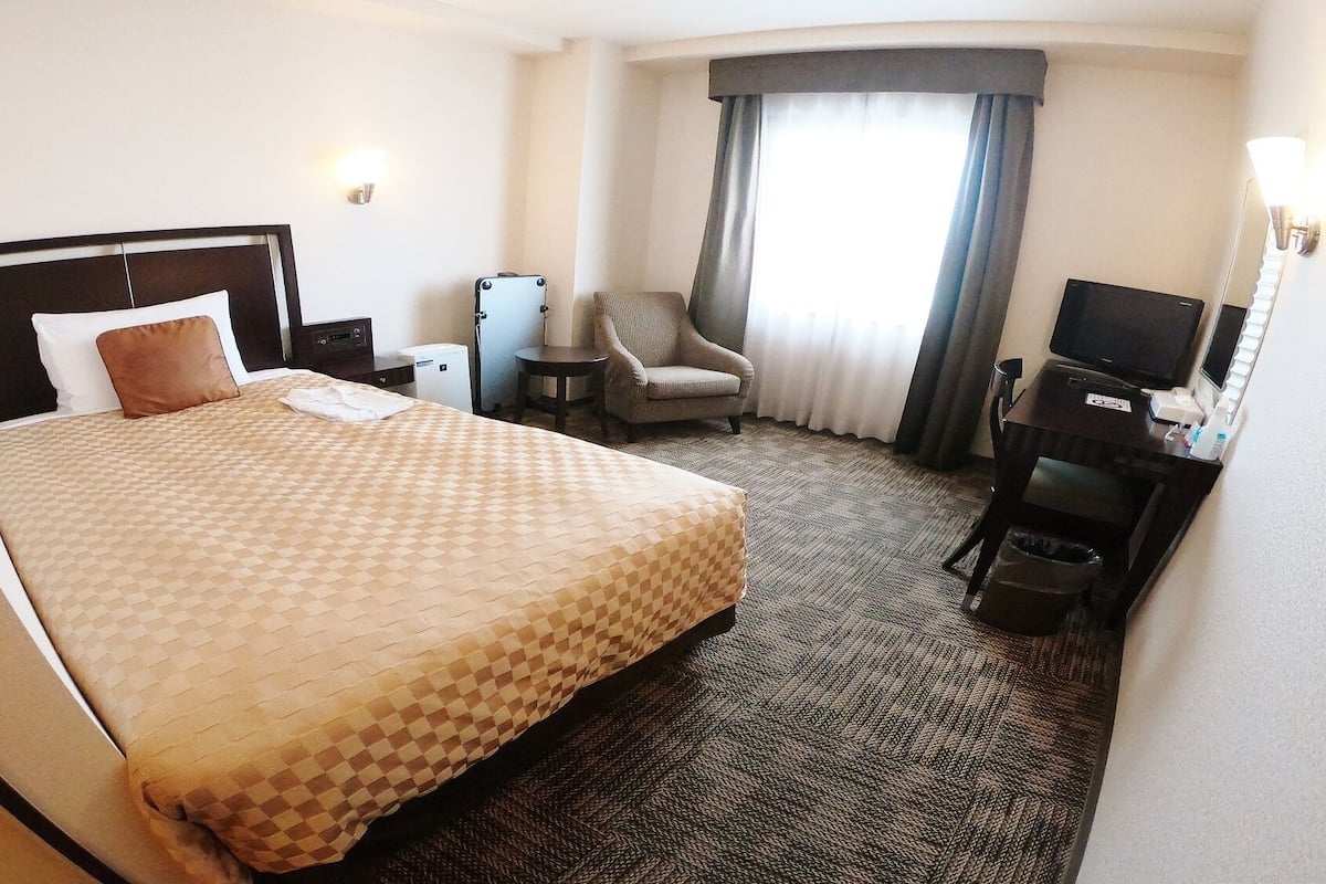 Une chambre d’hôtel avec un grand lit, une chaise, un bureau avec une télévision et une petite table avec une lampe.
