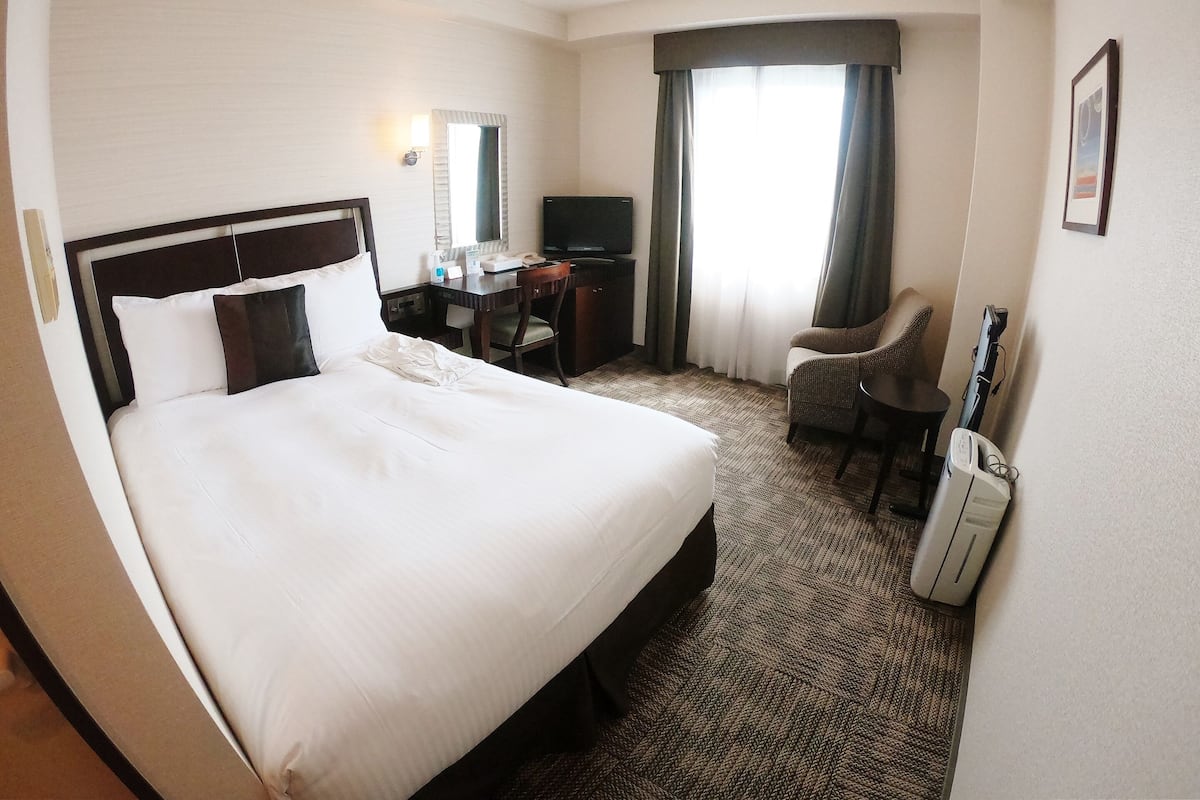 A hotel room with a large bed, a desk, a chair, a television, and a window with curtains.