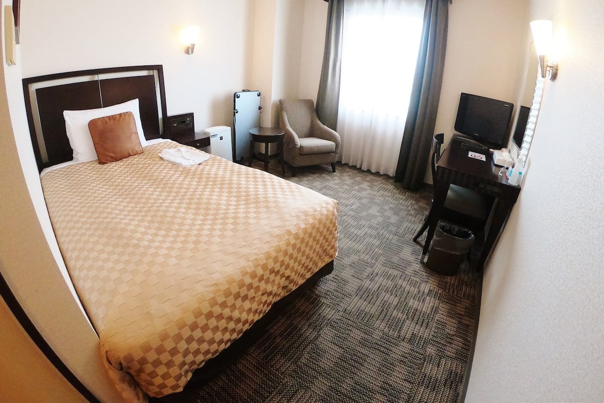 A hotel room with a large bed, a desk with a computer, a chair, a small table, and a TV.