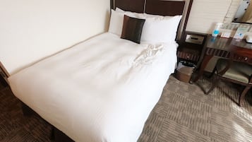 A neatly made bed with white linens, a wooden headboard, and a small bedside table with a bottle and a tissue box.