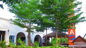 A stone wall with a sign for a room and coffee, a thatched-roof structure, and a building with arched windows. - Koh Tao Toscana (Koh Tao)