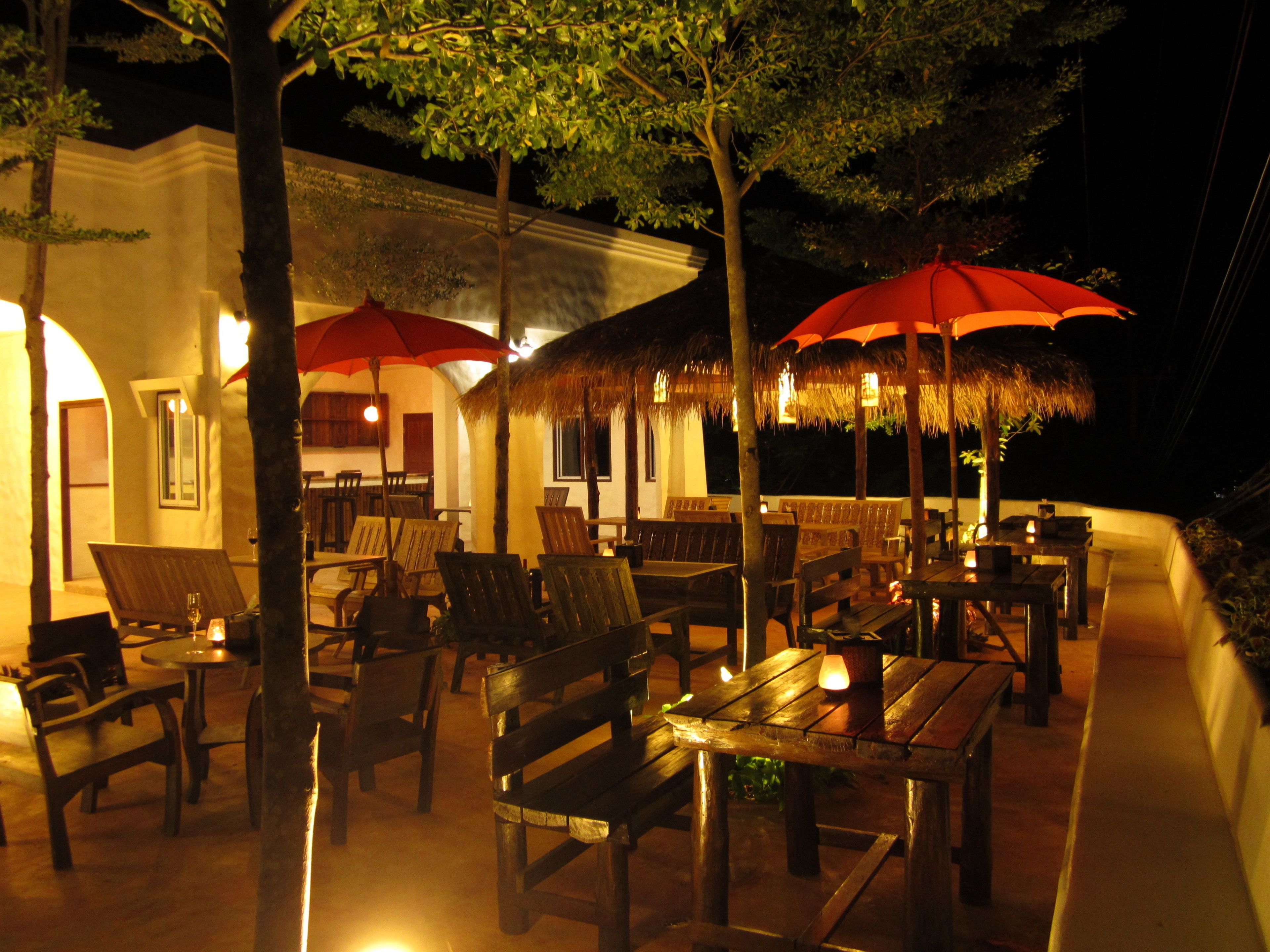 An outdoor dining area with wooden furniture and red umbrellas.