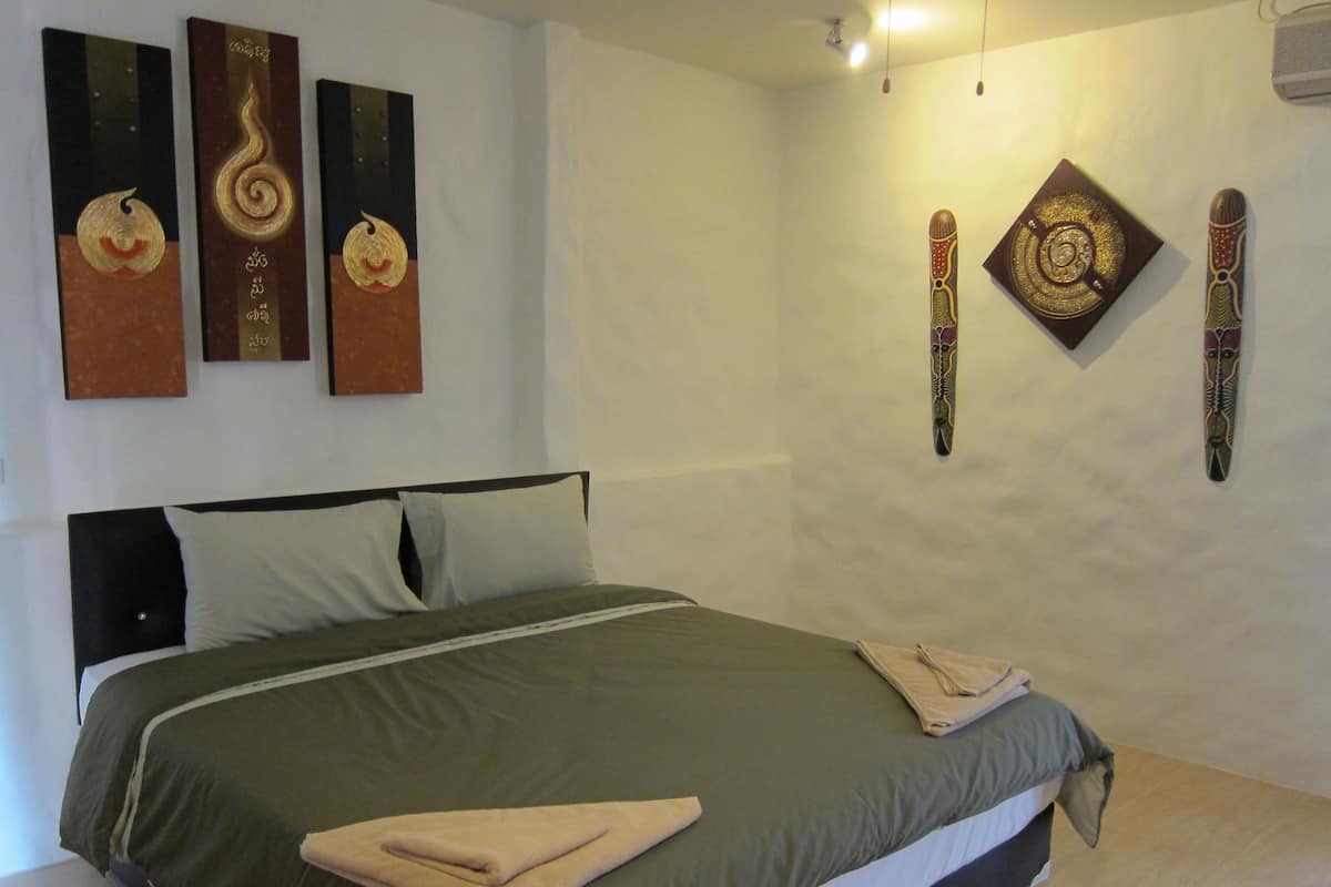 Cama bem arrumada com colcha verde, almofadas brancas e uma toalha dobrada ao lado.