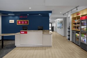 A reception area with a blue wall, a reception desk, and a 'Hello Denver' sign. There are two computer monitors, a refrigerator with snacks, and a 'Just chillin'' sign. - TownePlace Suites by Marriott Denver Airport at Gateway Park (Denver)