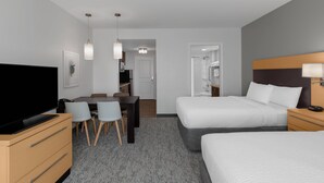 Habitación de hotel con cama, mesita de noche, televisión, escritorio, sillas y piso alfombrado.