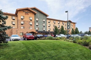 A hotel with a brick facade, multiple floors, and a parking lot with various cars. - TownePlace Suites by Marriott Denver Airport at Gateway Park (Denver)