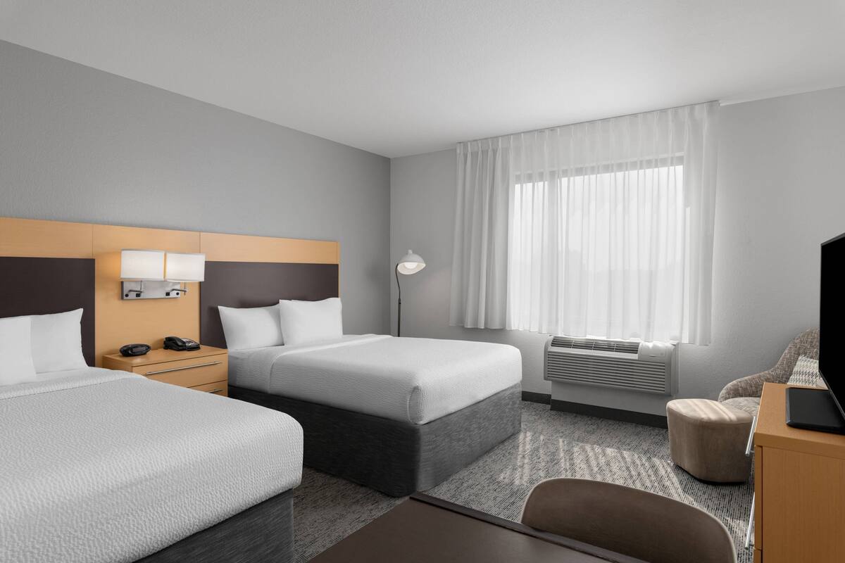 Habitación de hotel con dos camas, un escritorio, una silla, un televisor y una ventana con cortinas.