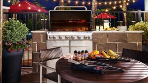 Un área de barbacoa al aire libre con una parrilla, asientos y luces colgantes.