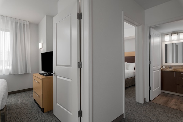 Habitación de hotel con cama, televisión, escritorio y baño con espejo y lavamanos.
