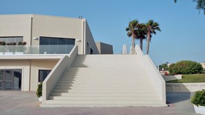 Un edificio moderno con una escalera que conduce a un balcón, rodeado de palmeras y follaje.