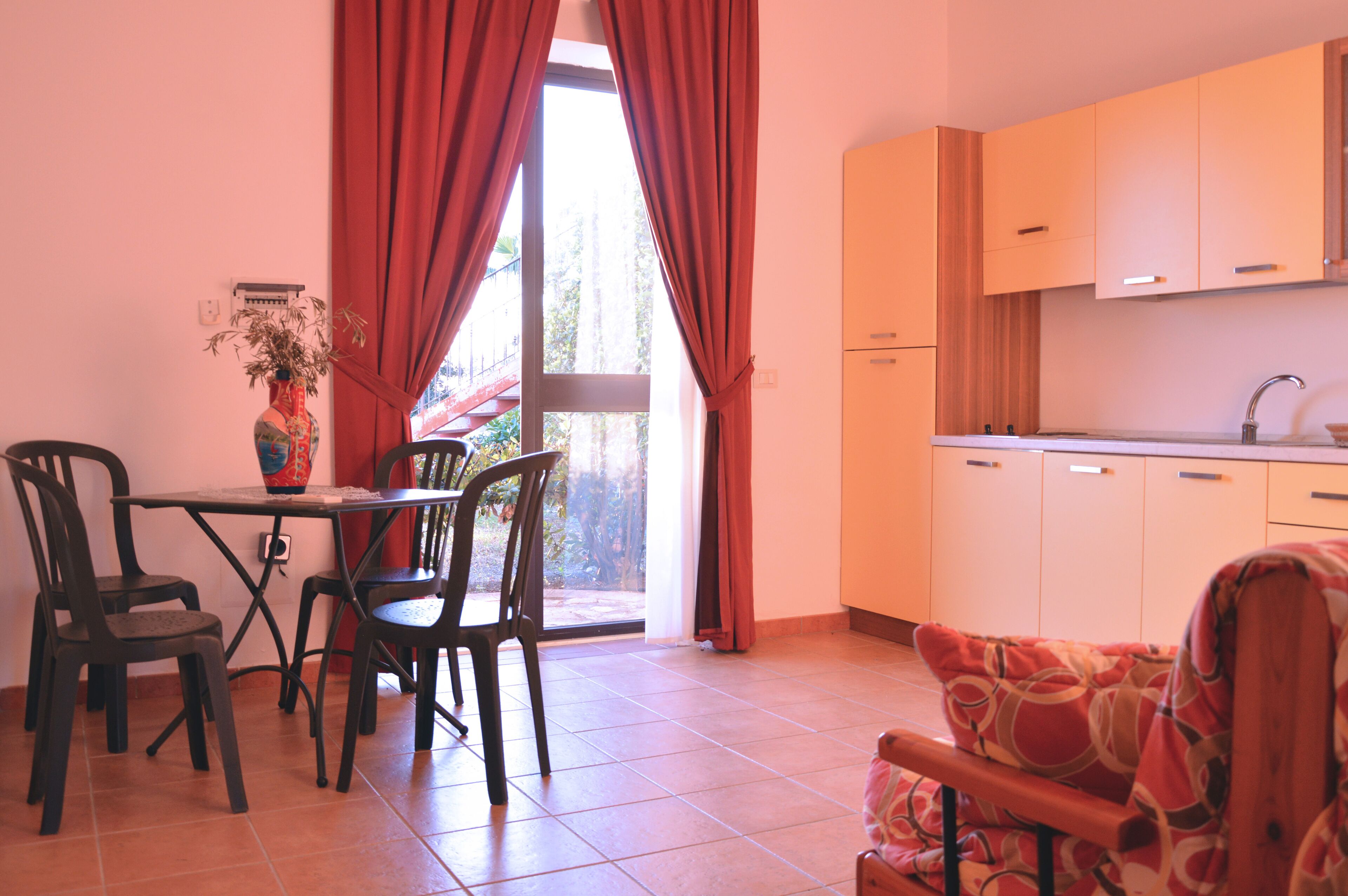 A dining area with a table and chairs, a kitchen with cabinets, and a window with curtains.