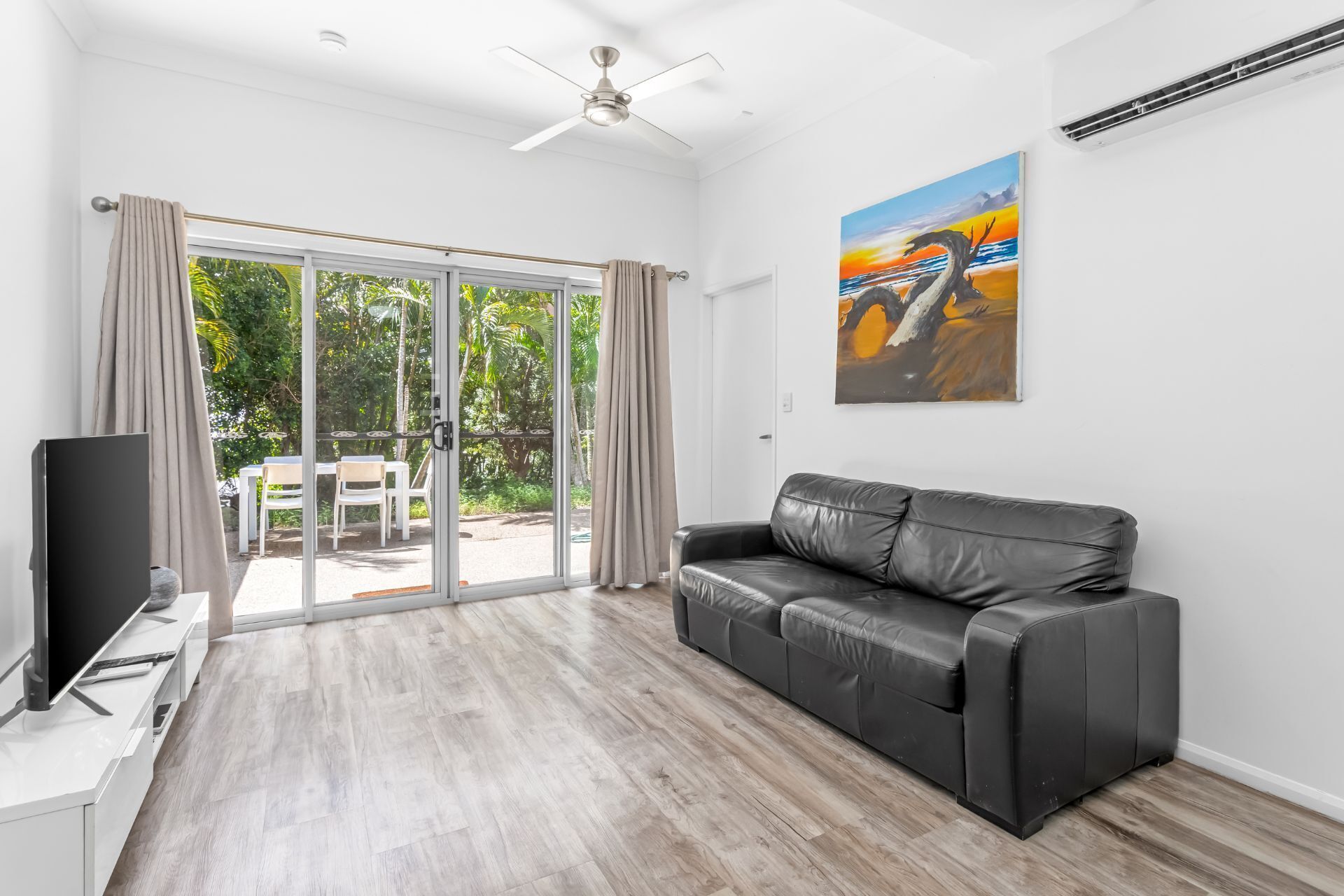 A modern living room with a black leather sofa, a flat-screen TV, and a painting of a sunset.