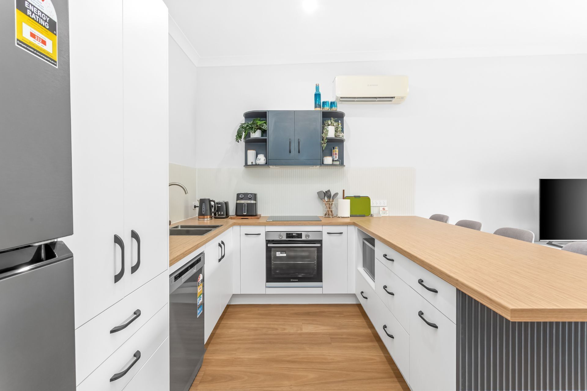 Una cocina moderna con armarios blancos, encimera de madera, horno empotrado y lavavajillas.