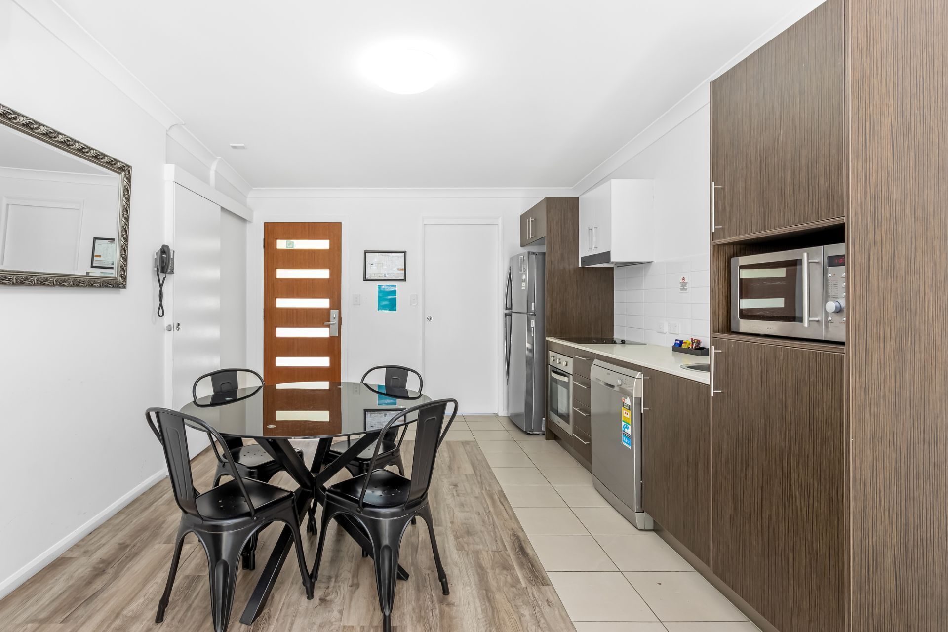 Une cuisine moderne avec un coin repas, des meubles en bois, des appareils électroménagers en acier inoxydable et une table en verre.