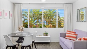 A modern living room with a dining area, large windows with blinds, a sofa, and a small table with chairs. - Rosslyn Bay Resort (Rosslyn)
