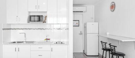 A modern kitchen with white cabinets, a microwave, a sink, and a refrigerator. There are two black bar stools and a white countertop.