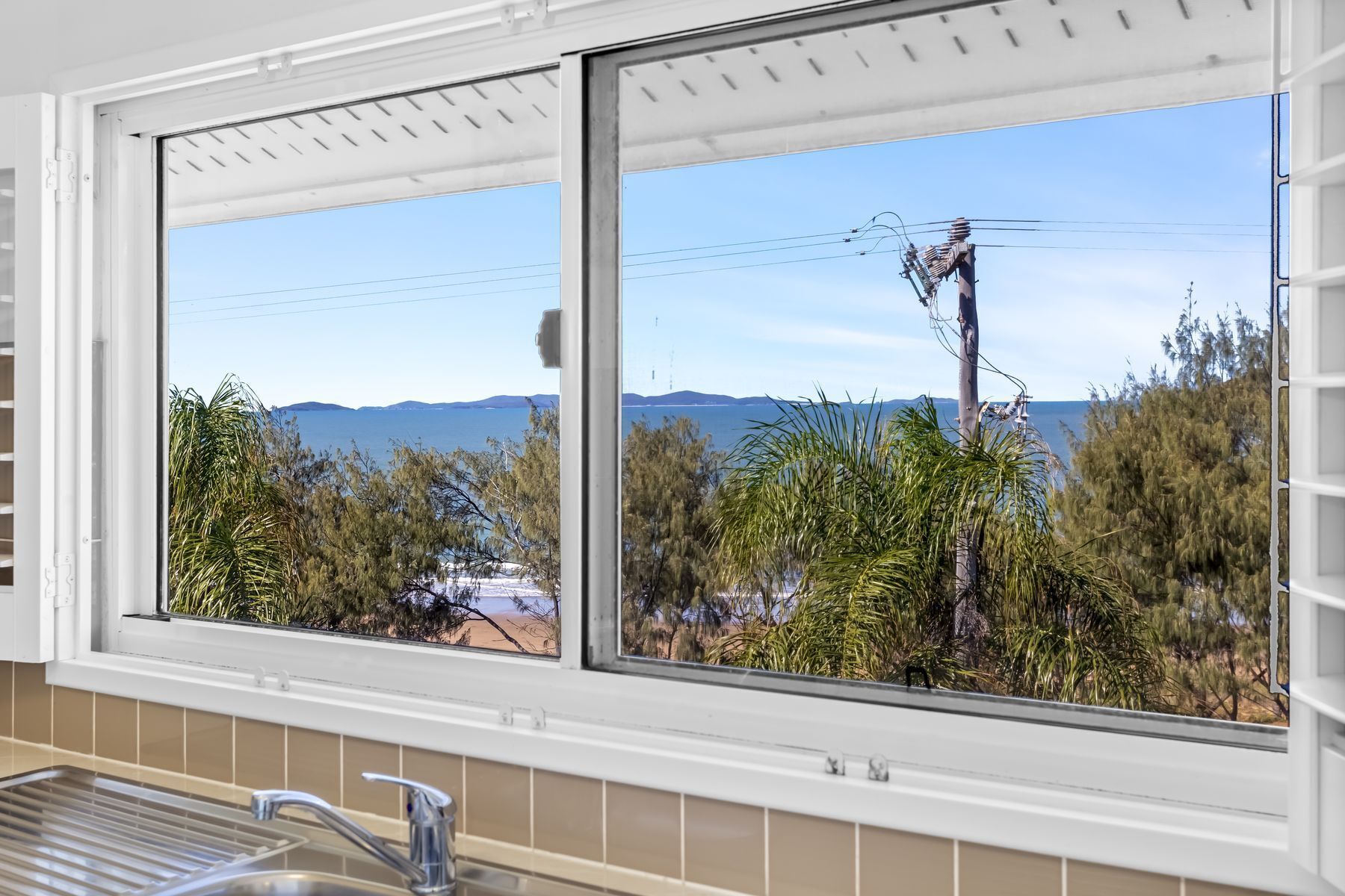 A kitchen with a window overlooking a landscape with trees and power lines.