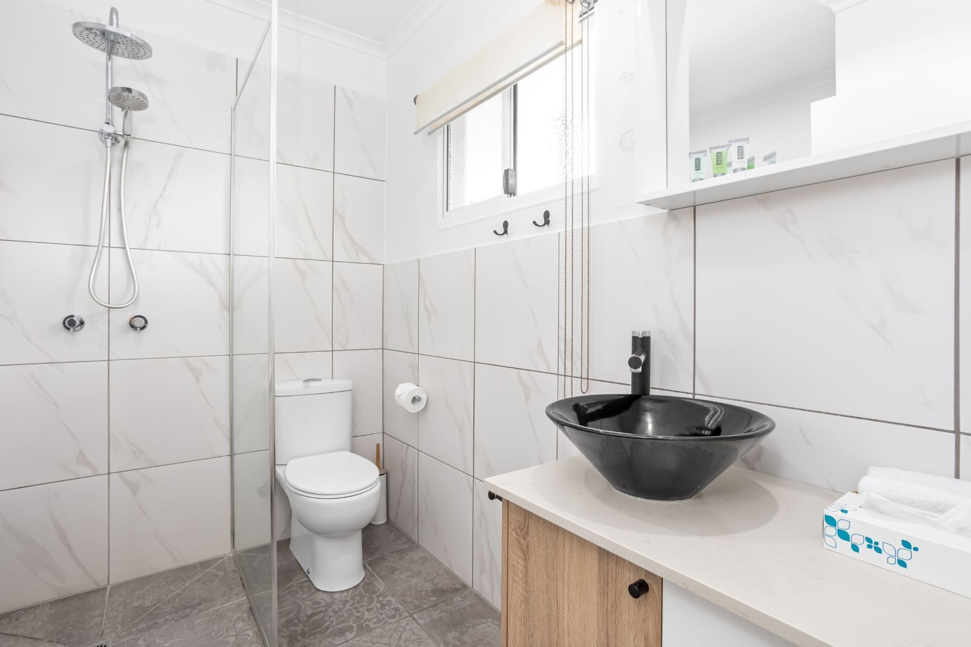 Un baño moderno con inodoro, ducha y un lavabo negro grande sobre un mostrador.