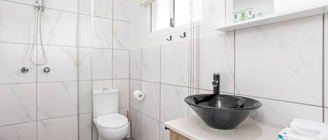 Un baño moderno con inodoro, ducha y un lavabo negro grande sobre un mostrador.