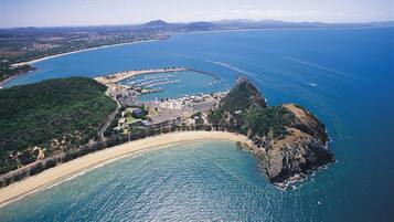 Vista aérea de una zona costera con playa, puerto deportivo y paisaje circundante.
