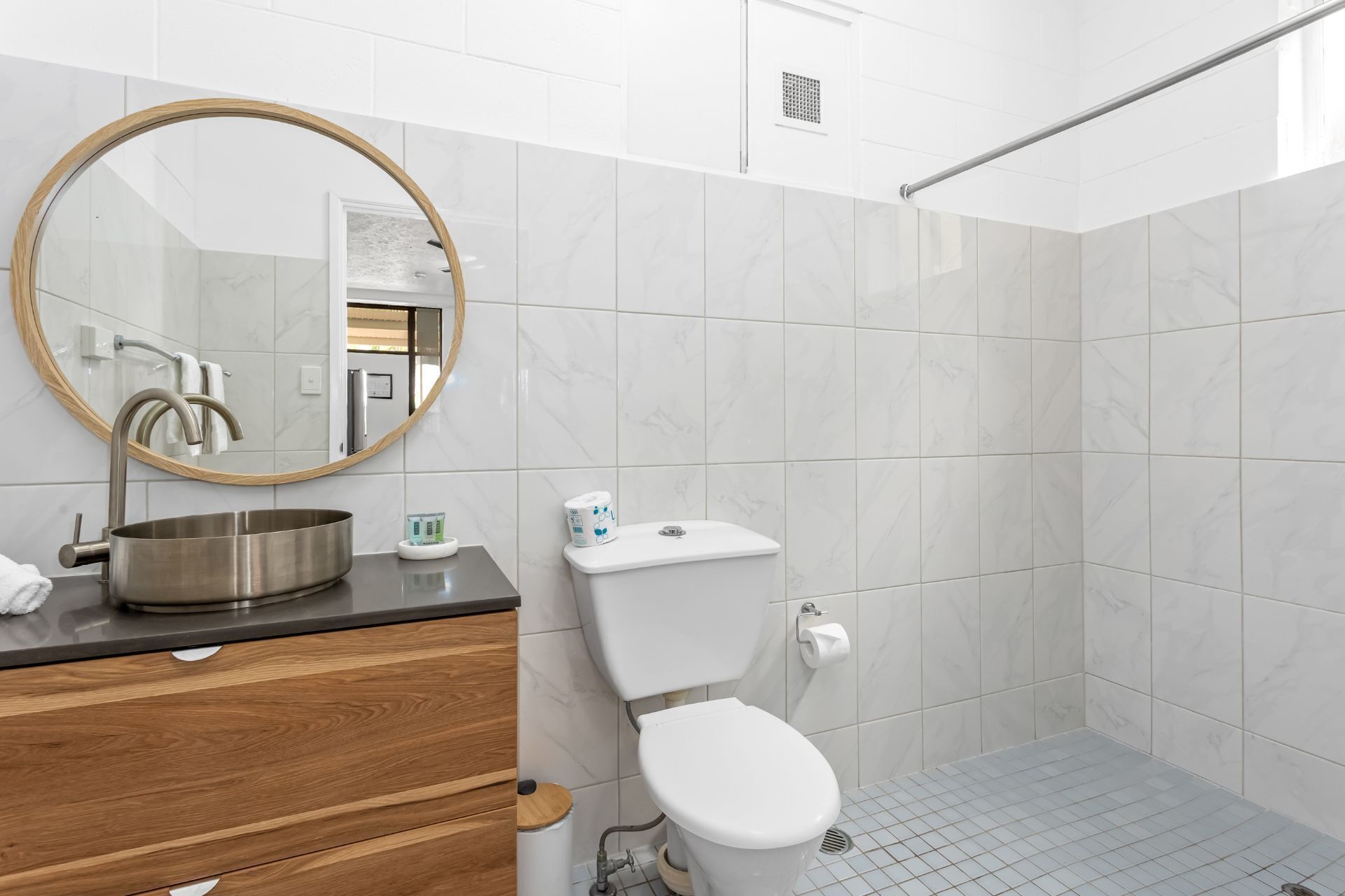 Une salle de bain moderne avec un miroir rond, un lavabo en acier inoxydable, des toilettes blanches et un espace douche.