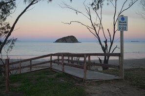 Pasarela de madera que lleva a una playa, con un cartel que indica el acceso a la misma.