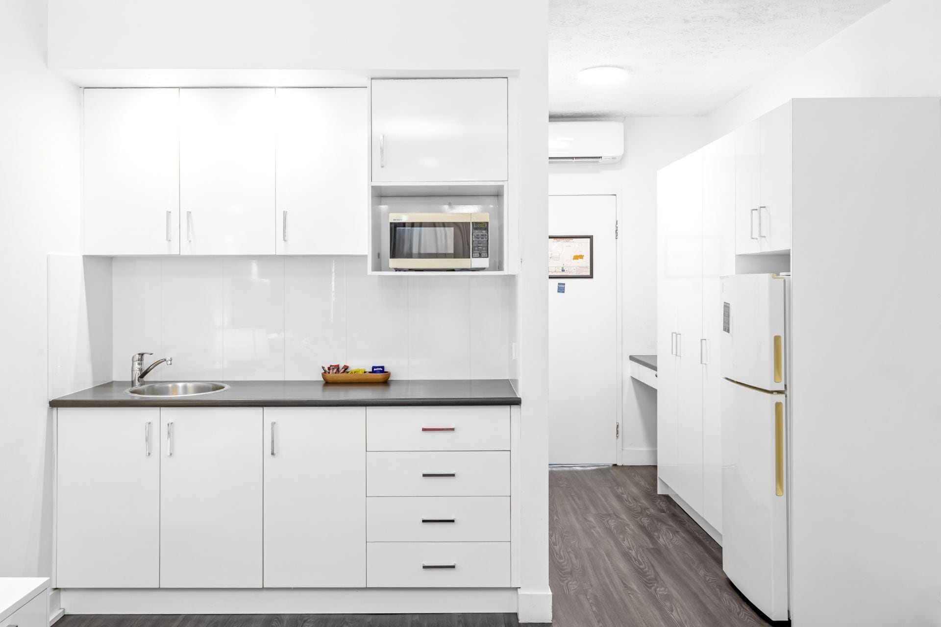 A modern kitchen with white cabinetry, a stainless steel sink, a microwave, and a refrigerator.