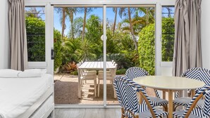 A room with a bed, a table with chairs, and a sliding glass door leading to a garden. - Rosslyn Bay Resort (Rosslyn)