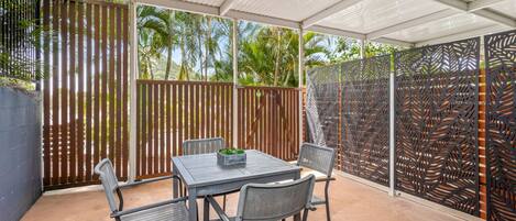 A covered patio with a table and chairs, a decorative fence, and a view of palm trees.