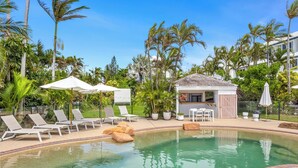 A pool area with lounge chairs, a small hut, and palm trees. - Rosslyn Bay Resort (Rosslyn)