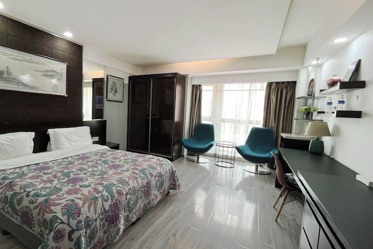 A hotel room with a large bed, two chairs, a desk, and a wardrobe.