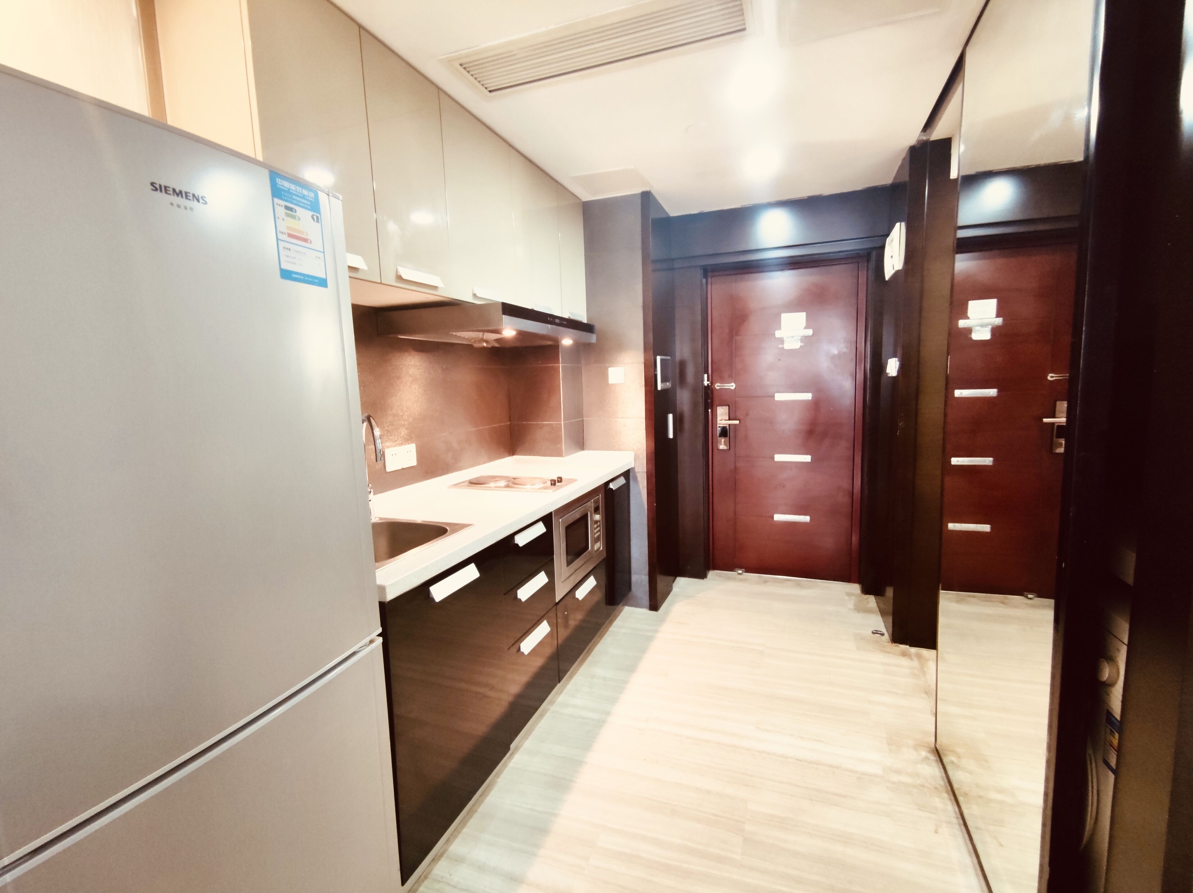 Una cocina moderna con un refrigerador Siemens, armarios de madera, un microondas y un lavadero de acero inoxidable.