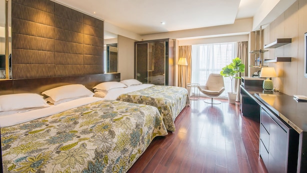 A hotel room with two beds, a desk, a chair, a potted plant, and a large mirror.