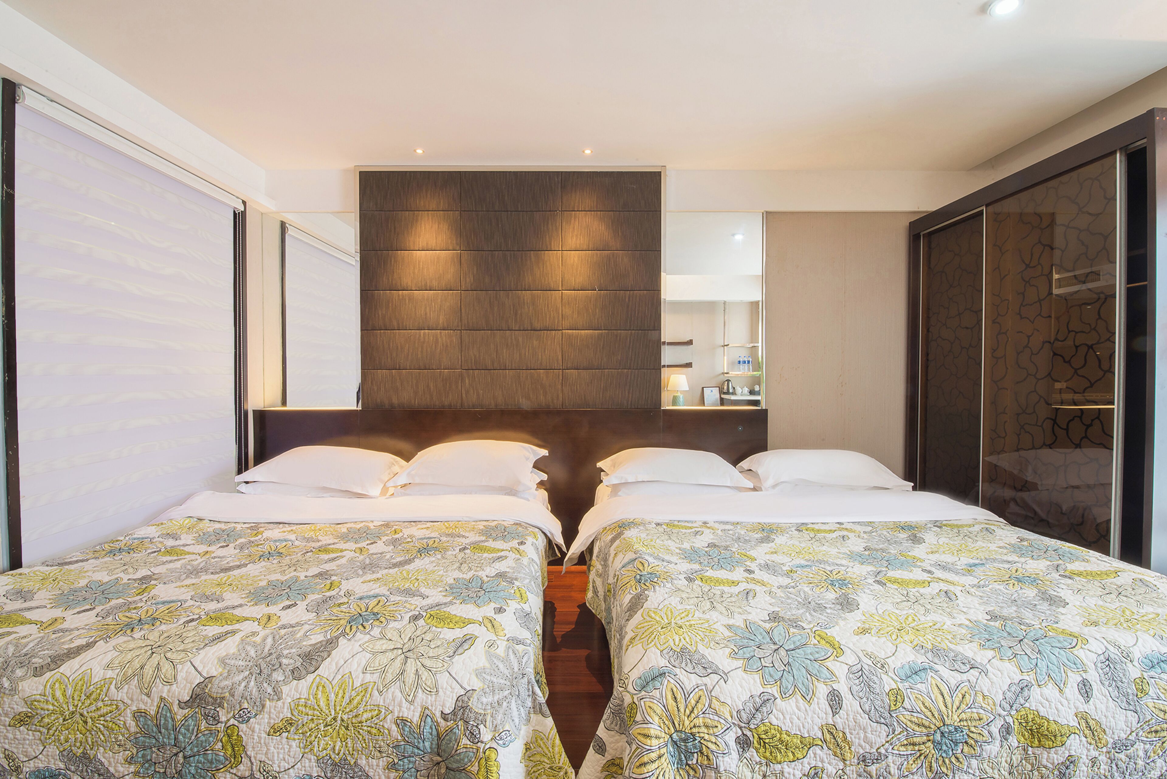 Quarto de hotel com duas camas, cabeceira de madeira, um espelho grande e vista para a cidade.