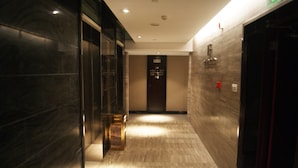 A hallway with a marble floor and a glass door on the left. There is a sign with room numbers on the wall.