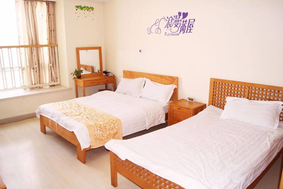 A hotel room with two beds, a wooden headboard, a nightstand, a mirror, and a window with curtains.