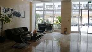 Eine moderne Lobby mit einem schwarzen Ledersofa, einem Glastisch mit Blumen und einem großen Fenster mit Blick auf geparkte Autos und Gebäude.