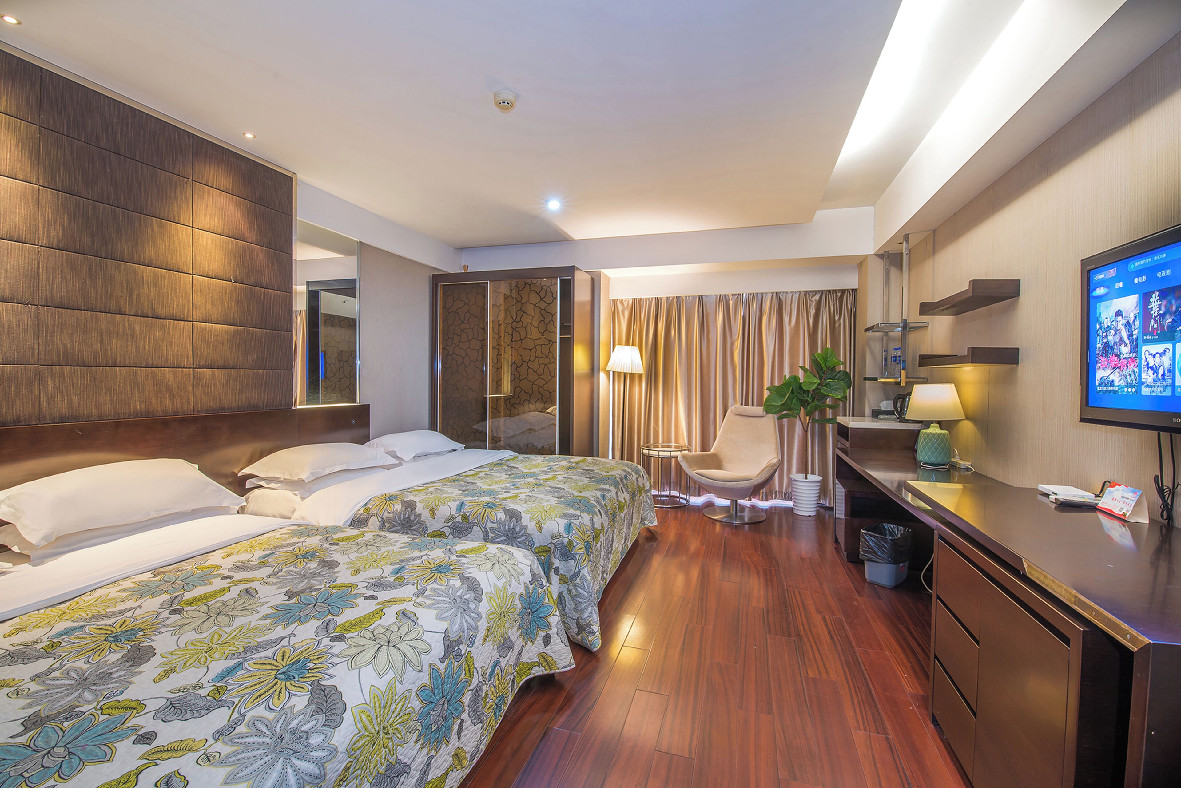 A hotel room with a large bed, a desk with a computer, a TV, and a plant.