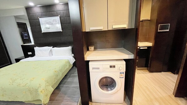 A compact hotel room with a bed, a washing machine, and a small kitchenette area. - Nanjing Kaibin Apartment Zhujianglu Muma (Nanjing)