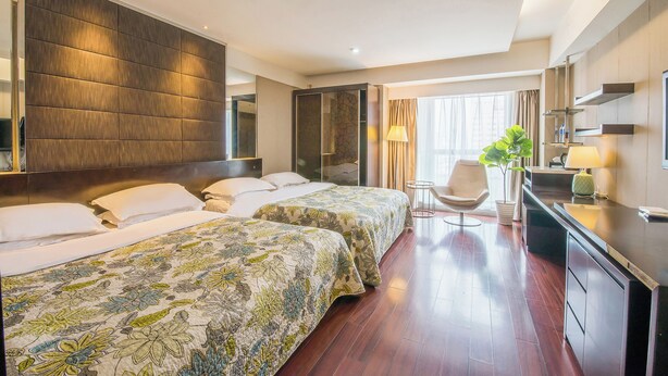 Ein Hotelzimmer mit zwei Betten, einem Schreibtisch, einem Sessel, einer Topfpflanze und einem großen Spiegel.