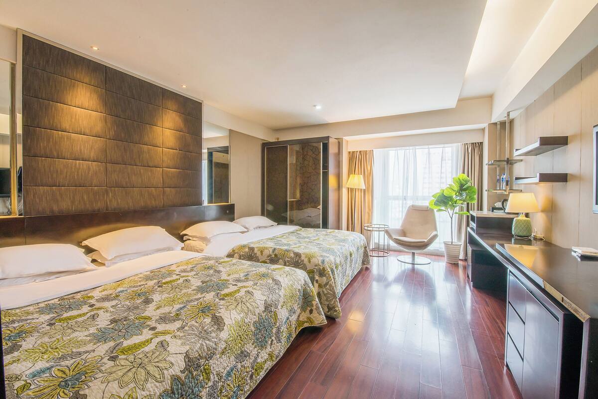 Une chambre d’hôtel avec deux lits, un bureau, une chaise, une plante en pot et un grand miroir.