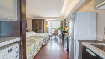 A hotel room with a bed, a chair, a washing machine, a refrigerator, and a sink.
