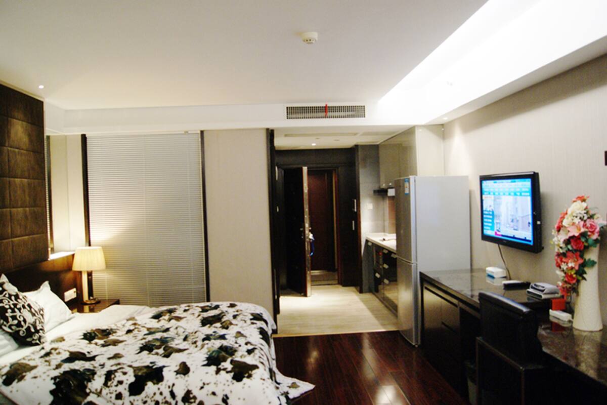 Une chambre d’hôtel avec un lit, un bureau, une télévision et une salle de bain visible à travers une porte ouverte.