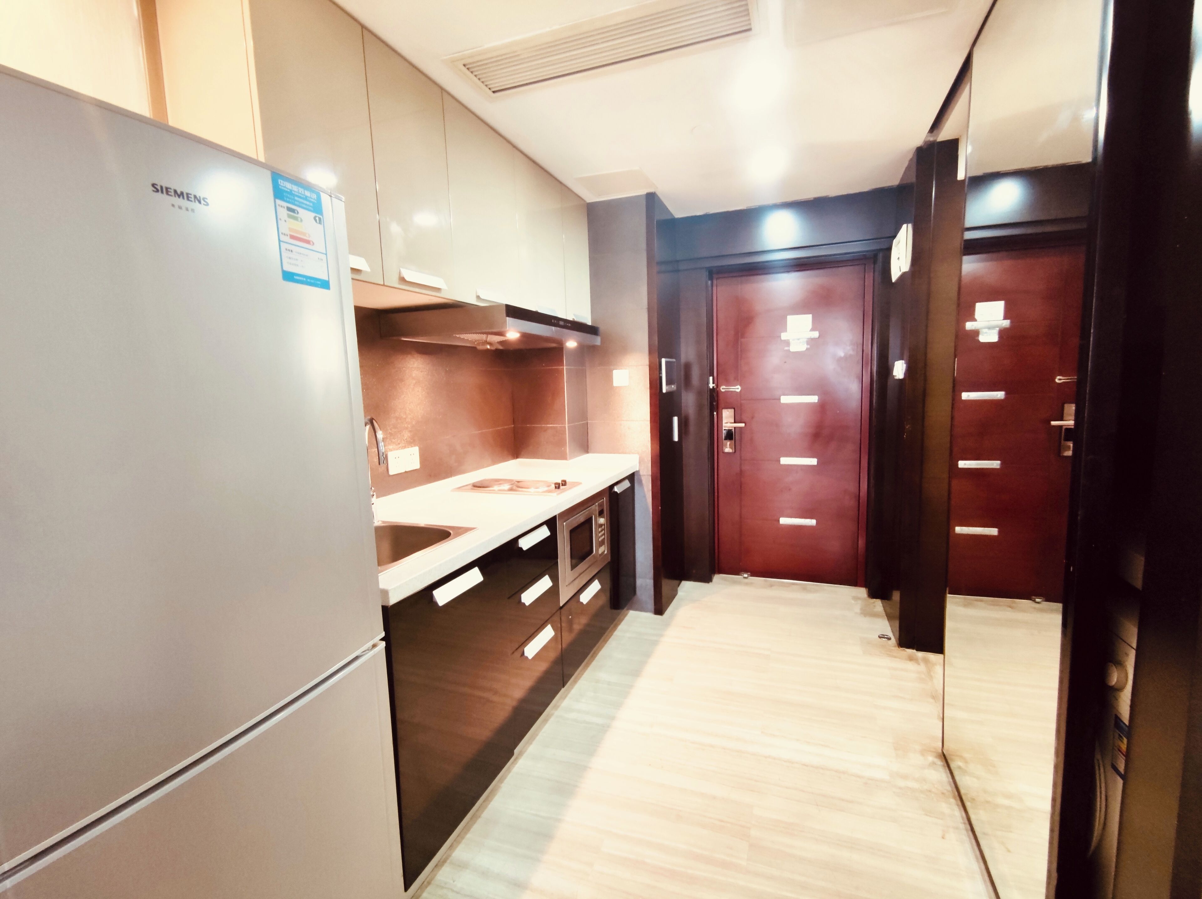 A modern kitchen with a Siemens refrigerator, wooden cabinets, a microwave, and a stainless steel sink.