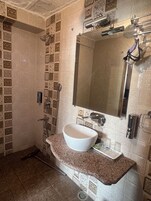A bathroom with a white sink, a mirror, and a shower area with a tiled wall.