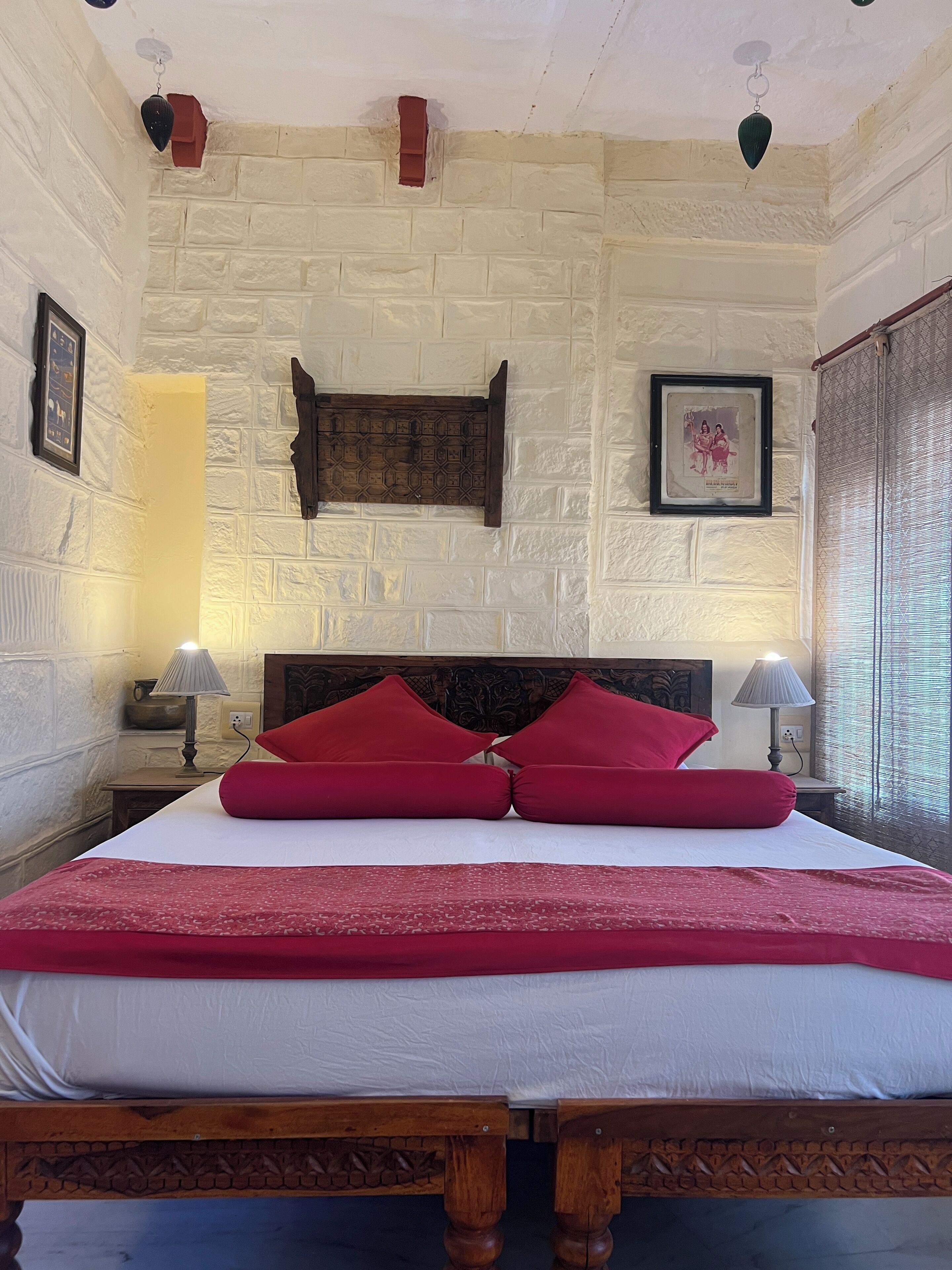 A bed with red pillows, a wooden headboard, and a white wall with a brick pattern. There are two bedside lamps and a framed picture on the wall.