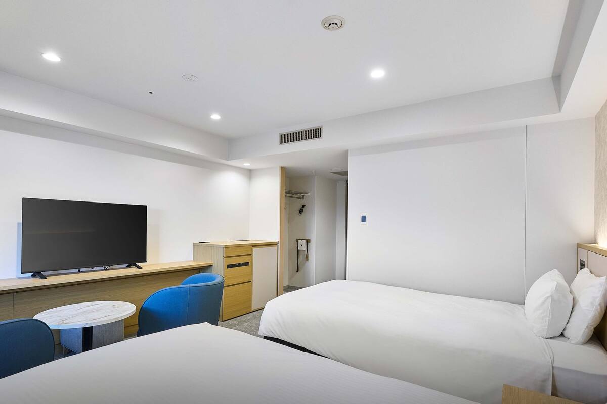 A modern hotel room with two beds, a flat-screen TV, a small round table, and a desk.