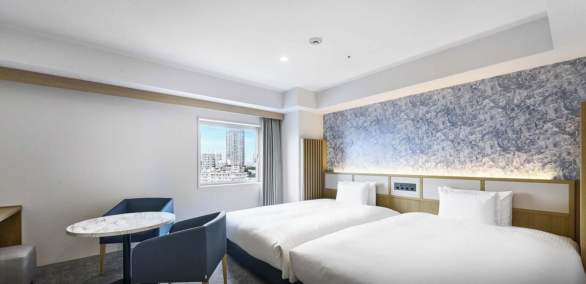 A hotel room with two beds, a small table, and a chair.