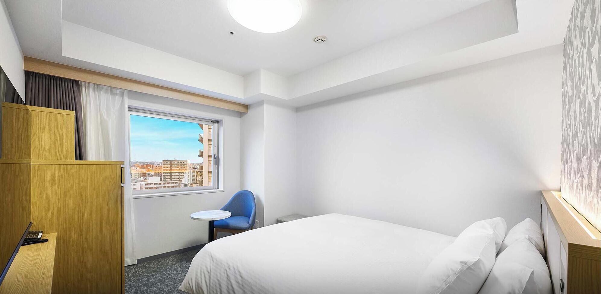 Habitación de hotel con cama, escritorio, silla y ventana con vista a la ciudad.